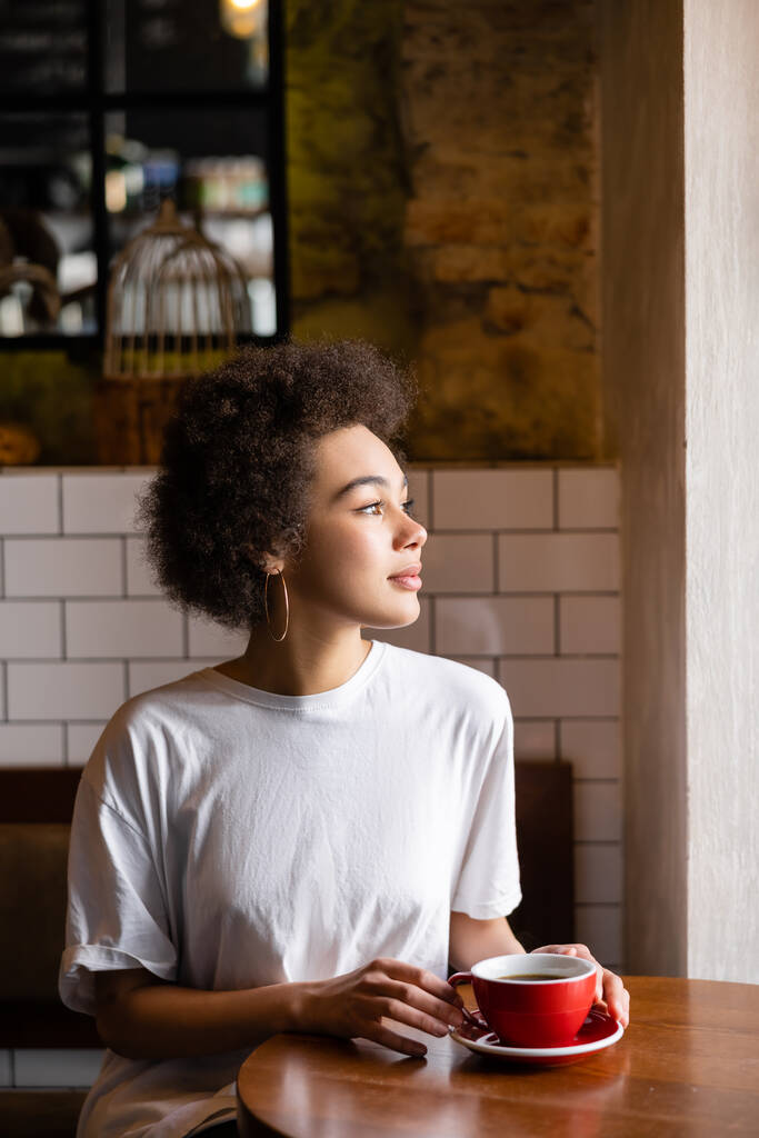 african american woman in hoop earrings and white t-shirt holding cup of coffee - Fotoğraf, Görsel