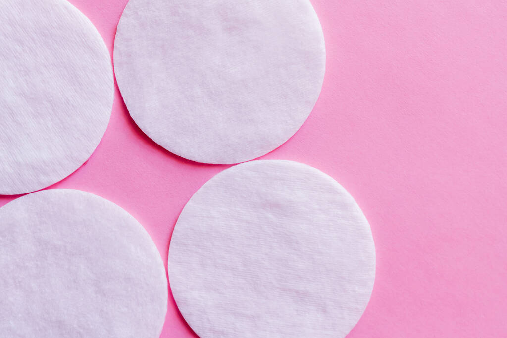 close up of white cotton pads on pink background, top view - Foto, afbeelding
