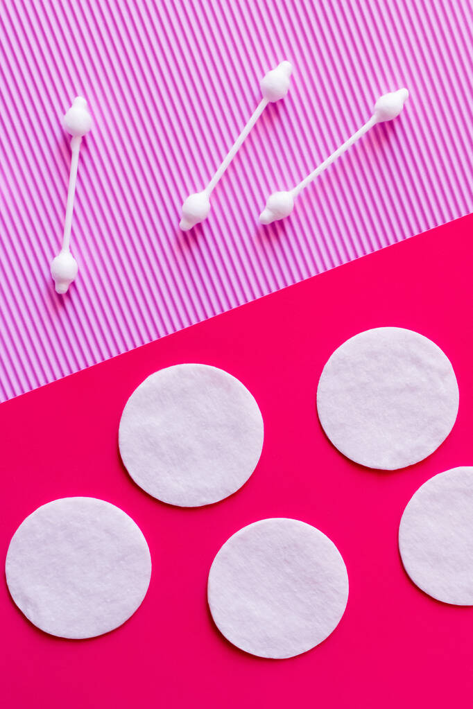 top view of white cotton pads and ear sticks on bicolor pink and violet background - Foto, afbeelding