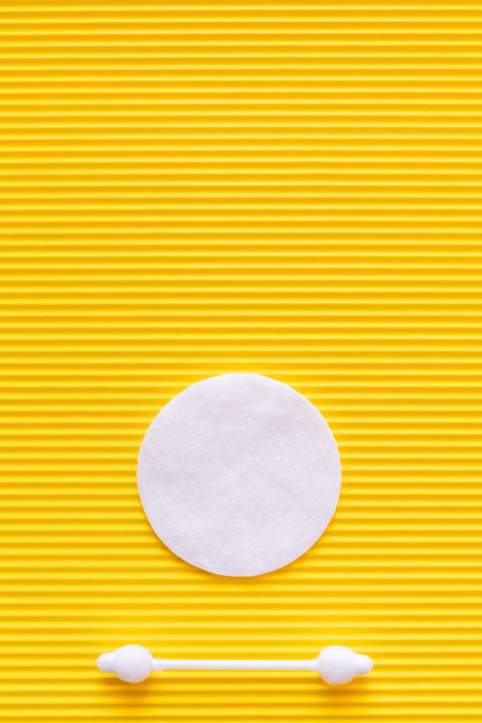top view of white cotton pad and ear stick on yellow textured background - Foto, Imagem