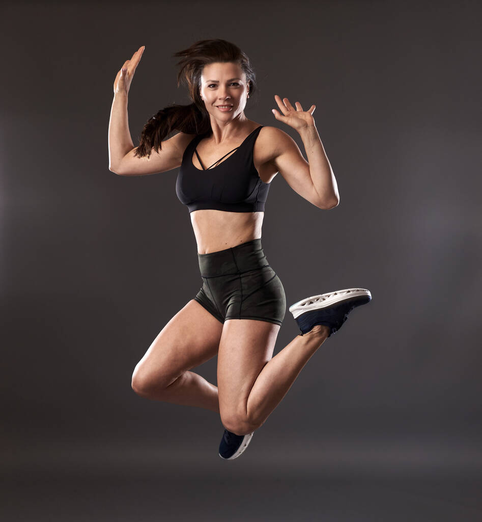 Athletic woman jumping high, freeze motion on gray background - Photo, Image