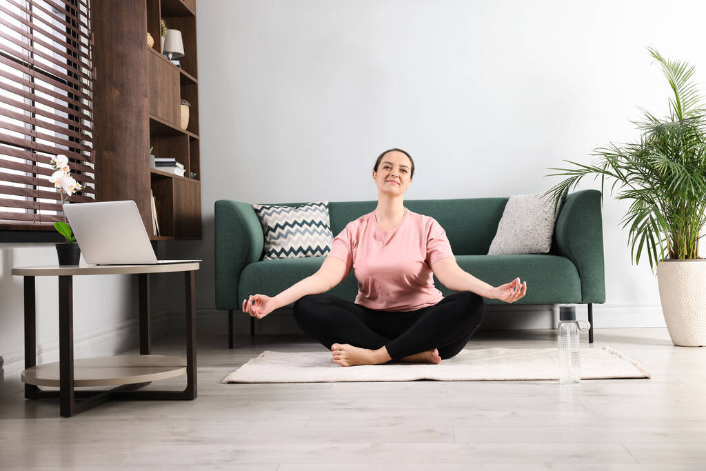 Надмірна вага жінки, що медитує на килимі вдома
 - Фото, зображення