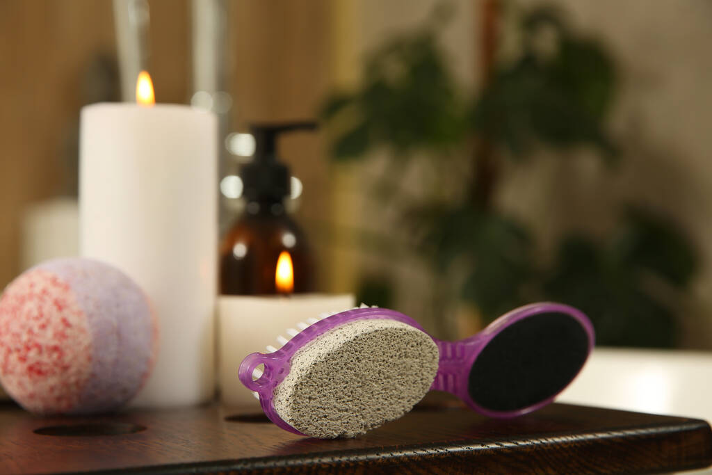 Pedicure tool with pumice stone and foot file near burning candles on wooden caddy in bathroom - Photo, Image