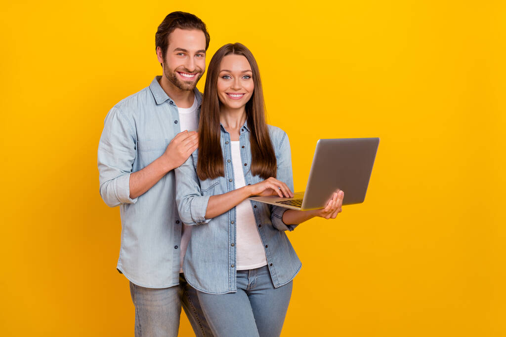 明るい黄色の背景に隔離されたノートパソコンの抱擁を使用してハンサムな美しい陽気なカップルの肖像画 - 写真・画像