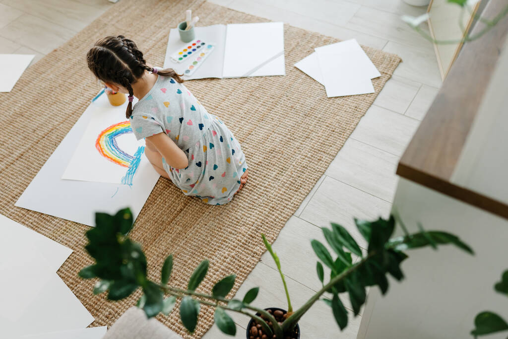 Child lying on floor and hold her draw with rainbow - Photo, Image