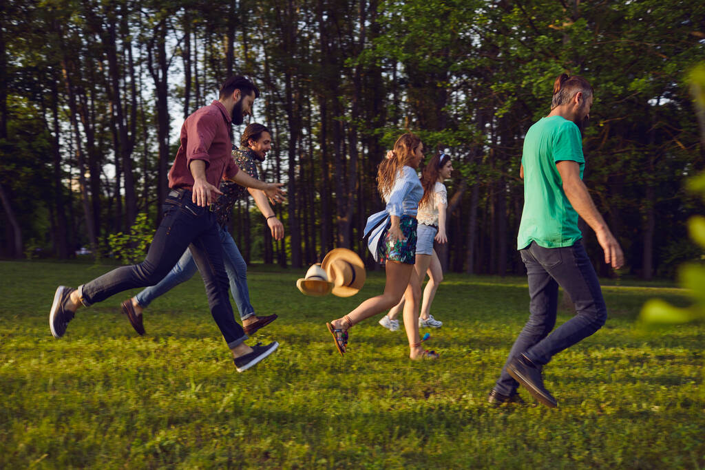 夏の公園で草の上を走る幸せな若者のグループ。休暇中の若者. - 写真・画像