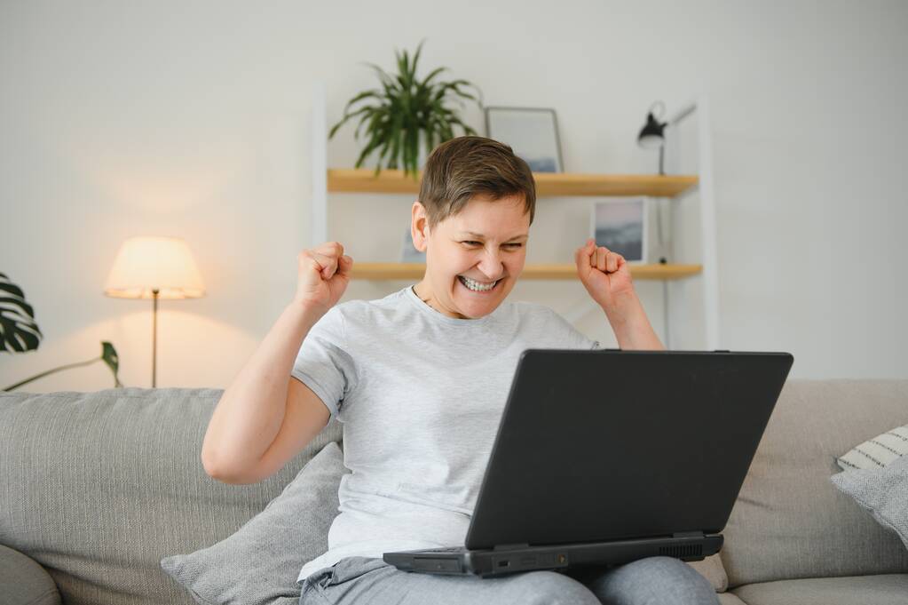 Technologia, ludzie i koncepcja komunikacji - Szczęśliwa seniorka z komputerem typu tablet posiadająca video czat w domu. Nowoczesny 50-letni babcia siedzieć relaks na kanapie w salonie za pomocą laptopa - Zdjęcie, obraz