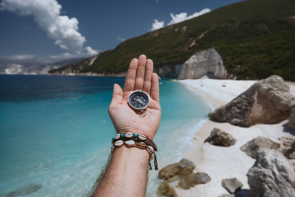 Рука держит компас на пляже в фоновом режиме. - Фото, изображение