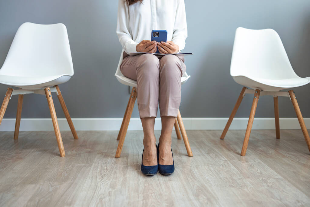 Молодая женщина ждет собеседования в приемной. Женщина, сидящая на стуле в приемной, перед собеседованием или встречей с потенциальными деловыми партнерами - Фото, изображение