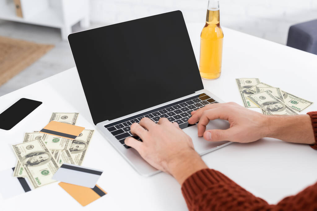 partial view of gambler typing on laptop with blank screen near dollars and credit cards - Foto, Imagem