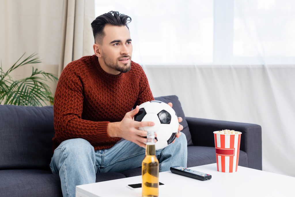 concentrated man with soccer ball watching championship on tv near popcorn and beer - Photo, Image