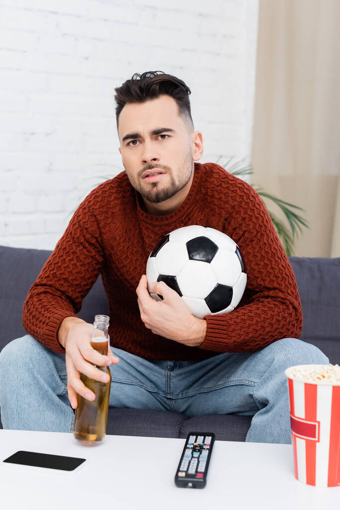 спортивный болельщик с футбольным мячом и просмотром пива на домашнем телевидении - Фото, изображение