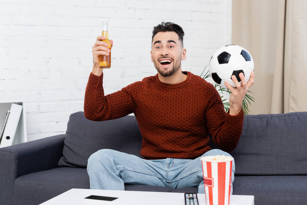 збуджений спортивний вентилятор з пивом і футбольним м'ячем дивитися гру на телебаченні вдома
 - Фото, зображення