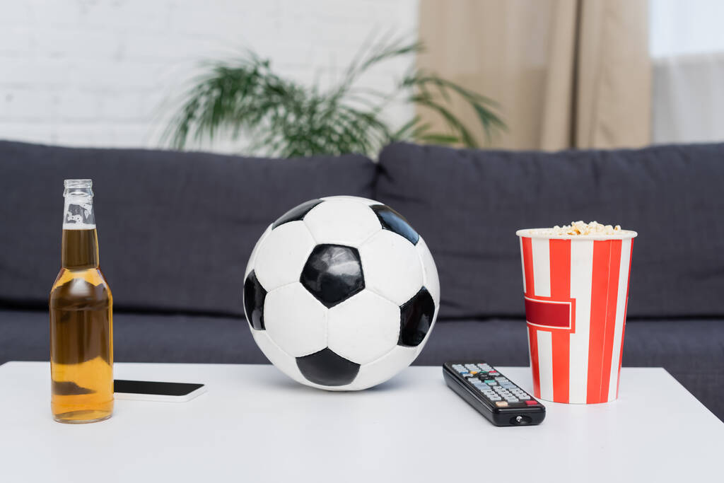 soccer ball, bucket of popcorn, tv remote controller, beer and smartphone on table - Foto, imagen