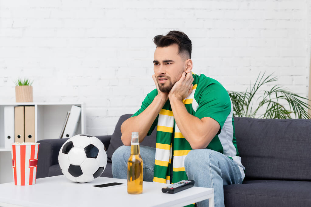 worried sports fan watching championship near soccer ball and beer at home - Photo, Image