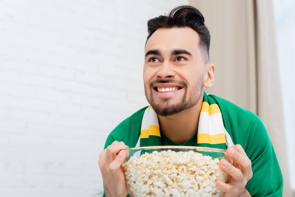 podekscytowany fan sportu trzymając miskę popcornu podczas oglądania mistrzostw w domu - Zdjęcie, obraz