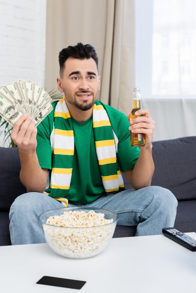 disappointed sports fan with money and beer watching match at home - Foto, immagini