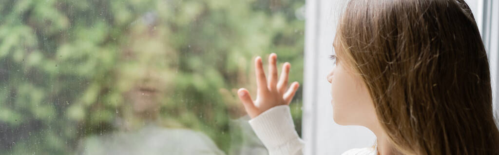 κορίτσι κοιτάζοντας μέσα από το παράθυρο και αγγίζοντας γυαλί με σταγόνες βροχής, πανό - Φωτογραφία, εικόνα