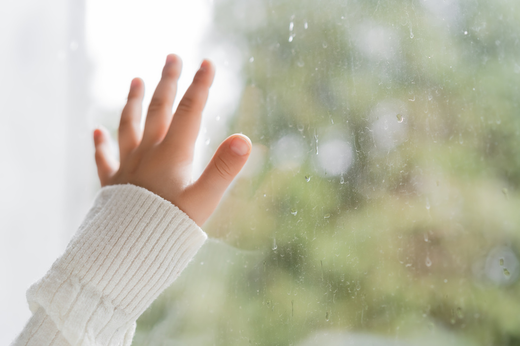 visão cortada da mão da criança perto da janela com gotas de chuva - Foto, Imagem