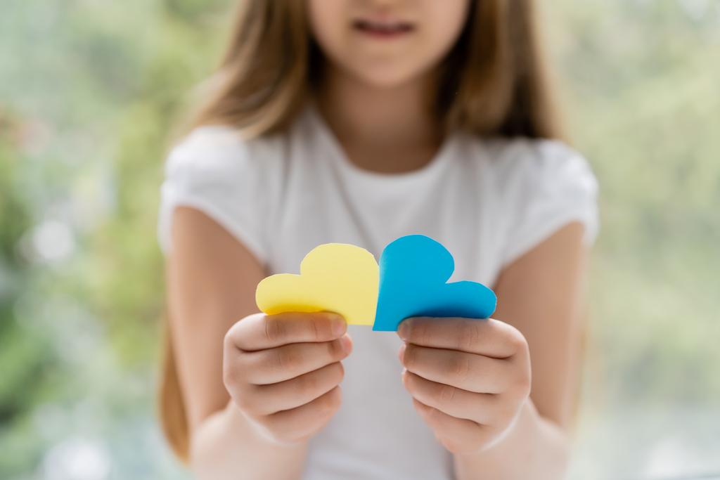 partial view of blurred girl holding blue and yellow paper hearts - 写真・画像