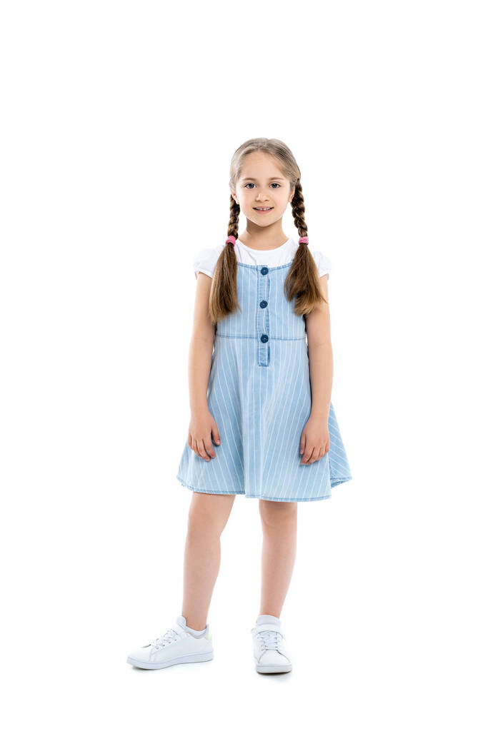 visão de comprimento total da menina em vestido de cinta azul sorrindo para a câmera enquanto em pé no branco - Foto, Imagem