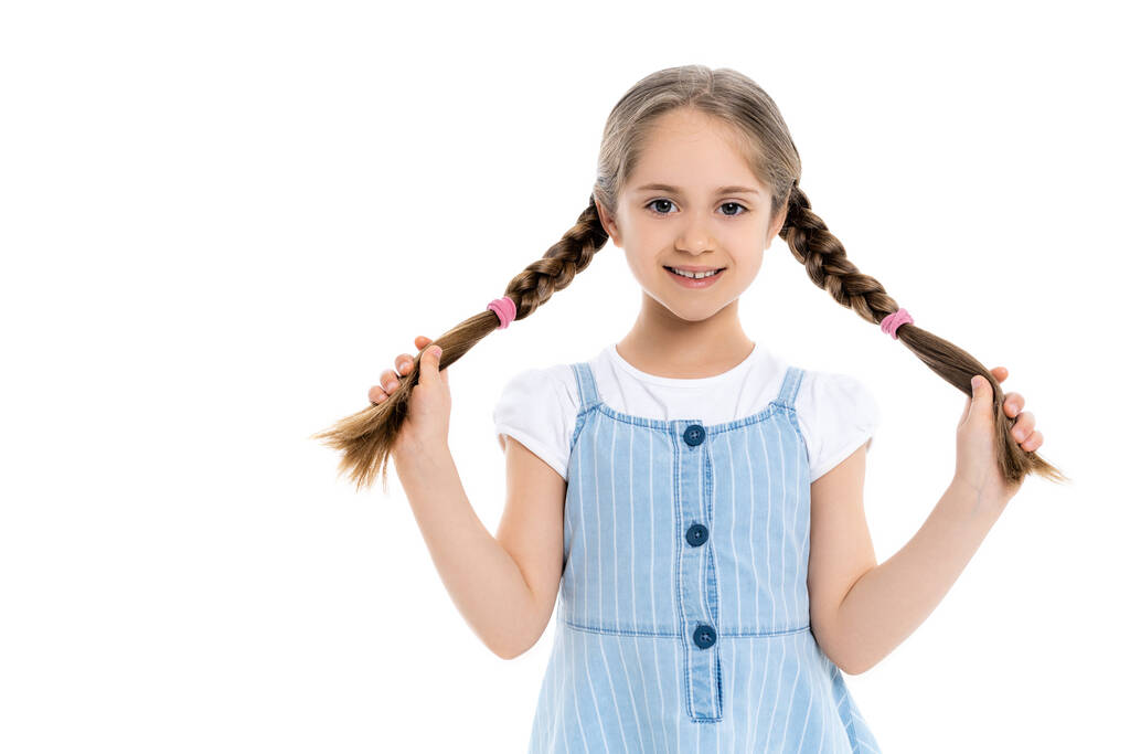 cheerful girl in blue strap dress holding braids isolated on white - Photo, Image