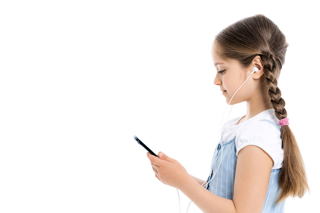 Seitenansicht von Mädchen in Kopfhörern mit Smartphone isoliert auf weiß mit Kopierraum - Foto, Bild