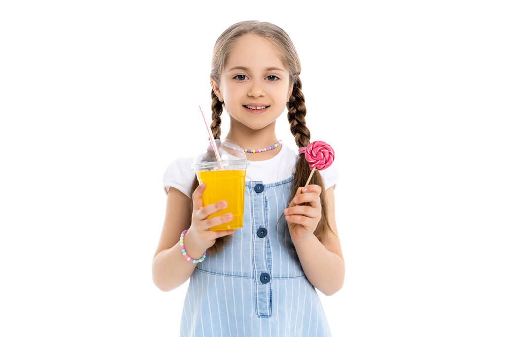 menina alegre com suco de laranja e pirulito olhando para a câmera isolada no branco - Foto, Imagem
