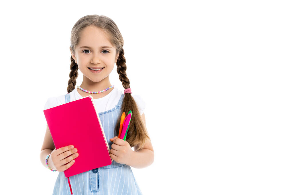 χαρούμενο κορίτσι με πολύχρωμα στυλό τσόχα και βιβλίο αντιγράφων κοιτάζοντας κάμερα απομονωμένη σε λευκό - Φωτογραφία, εικόνα
