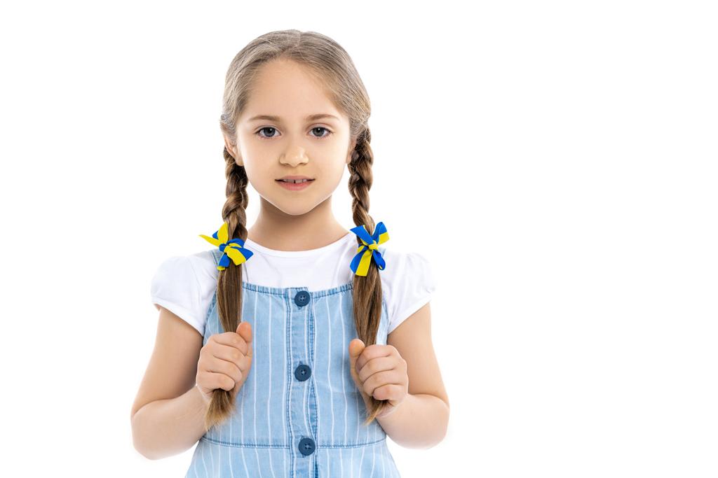 patriotic girl with blue and yellow ribbons on braids looking at camera isolated on white - Photo, Image