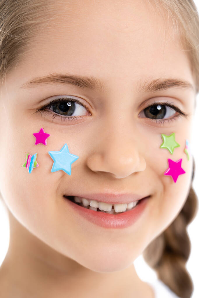 close-up portret van vrolijk meisje met kleurrijke sterren op gezicht glimlachen op camera geïsoleerd op wit - Foto, afbeelding