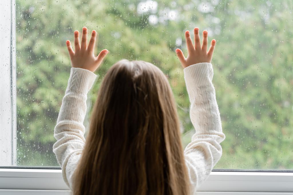 takaisin näkymä tyttö seisoo lähellä ikkunaa ja koskettaa lasia sadepisarat - Valokuva, kuva