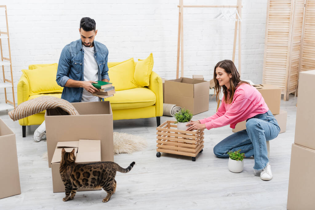 Positive interracial couple unpacking packages near bengal cat at home  - Zdjęcie, obraz