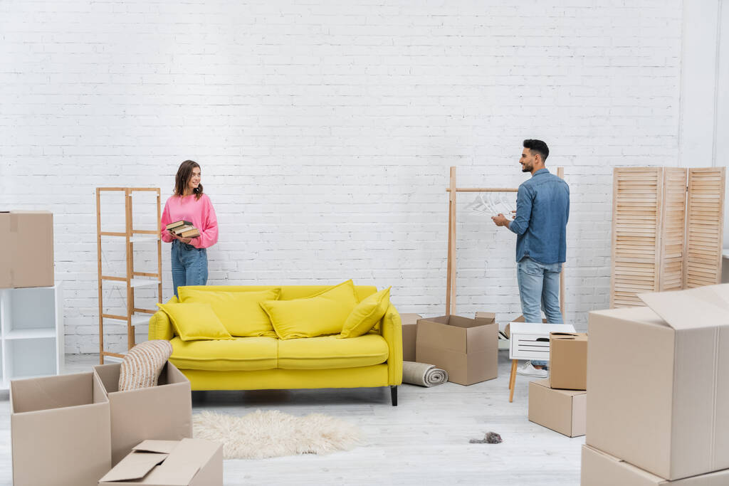 Cheerful multiethnic couple unpacking carton boxes in living room  - Foto, immagini
