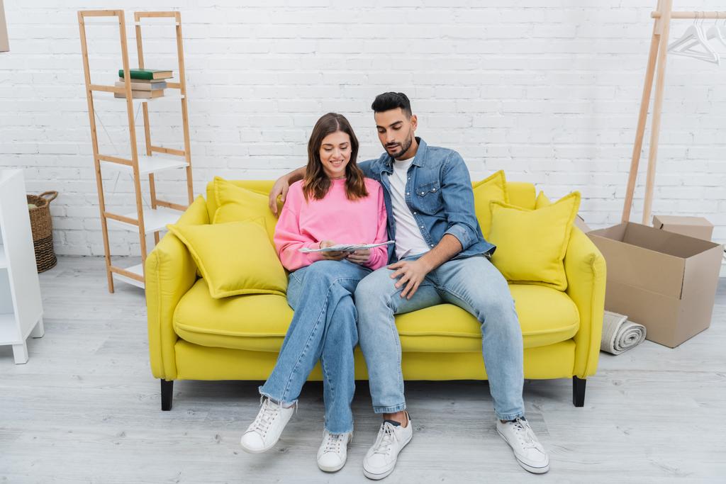 Smiling interracial couple holding color palette on couch at home  - Photo, Image