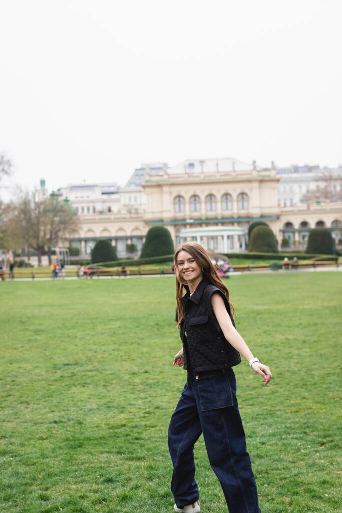 young joyful woman in sleeveless jacket in green park  - Photo, Image