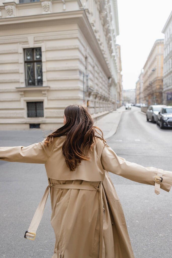widok z tyłu kobieta w płaszczu okopowym spacery z wyciągniętymi rękami w europejskim mieście  - Zdjęcie, obraz