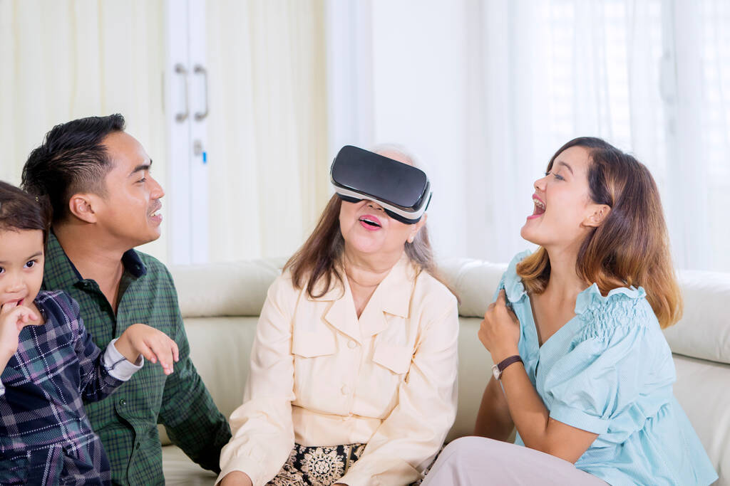 Mujer mayor con gafas VR mientras juega con su familia en la sala de estar. Disparo en casa - Foto, Imagen