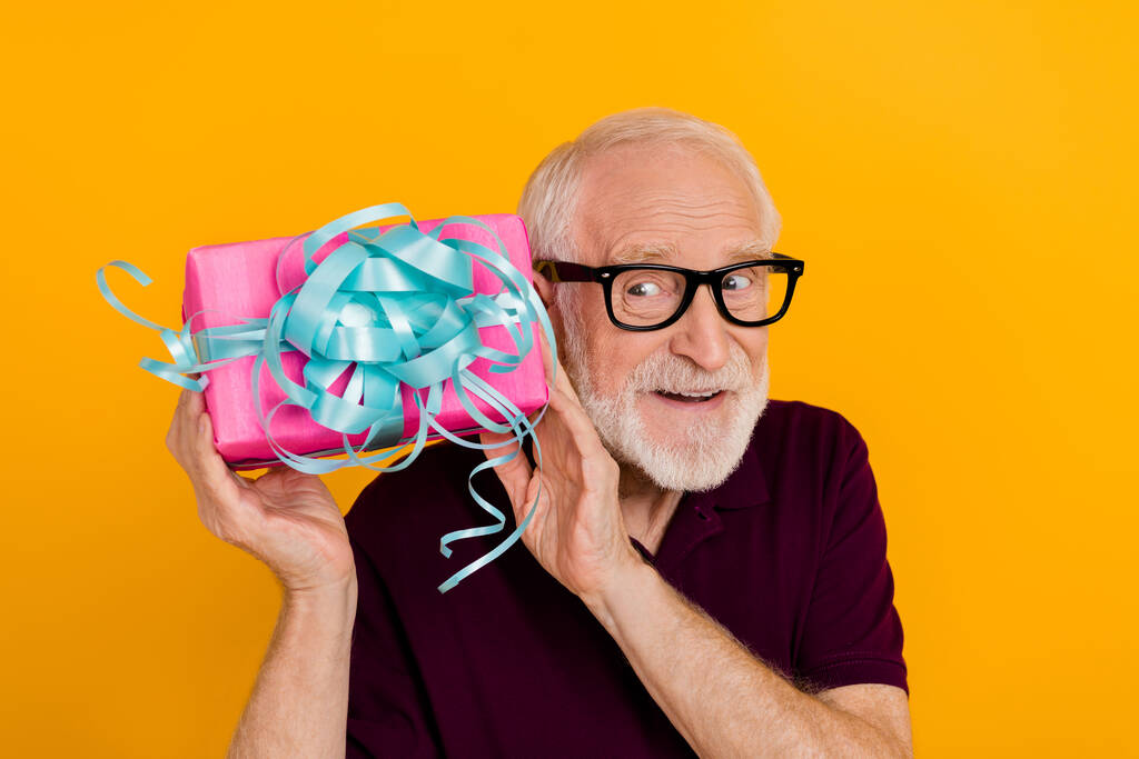 Photo of cheerful mature man look curious get present box ribbon isolated over yellow color background - 写真・画像