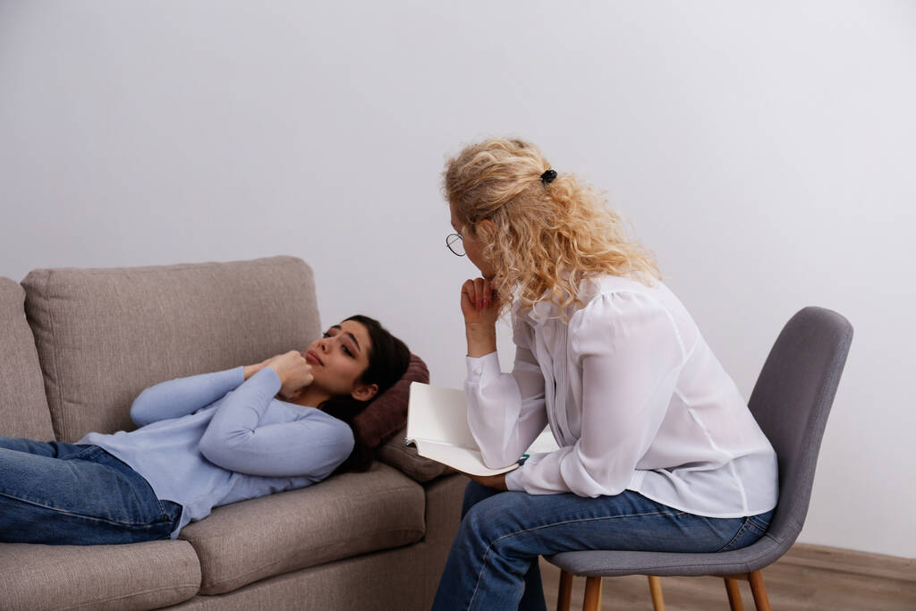 Psikolojik terapi seansında acı çeken genç bir kadın. Ofisteki psikologla müvekkili arasında geçen bir konuşma. Boşluğu kopyala, arkaplan. - Fotoğraf, Görsel