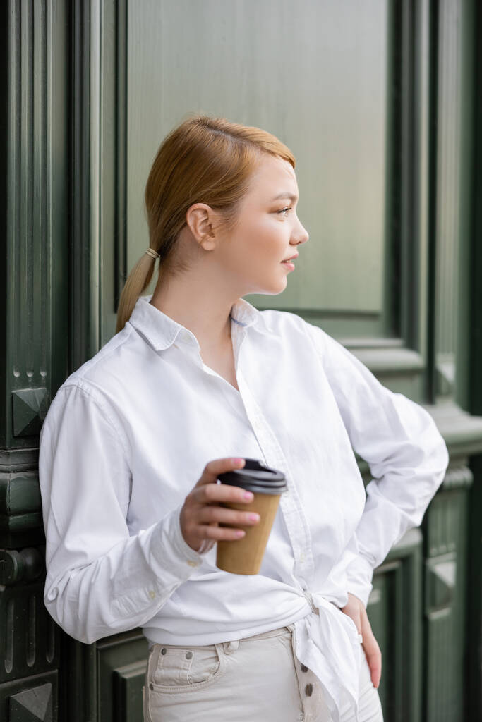 blonde woman with takeaway drink looking away near grey wall - Photo, Image