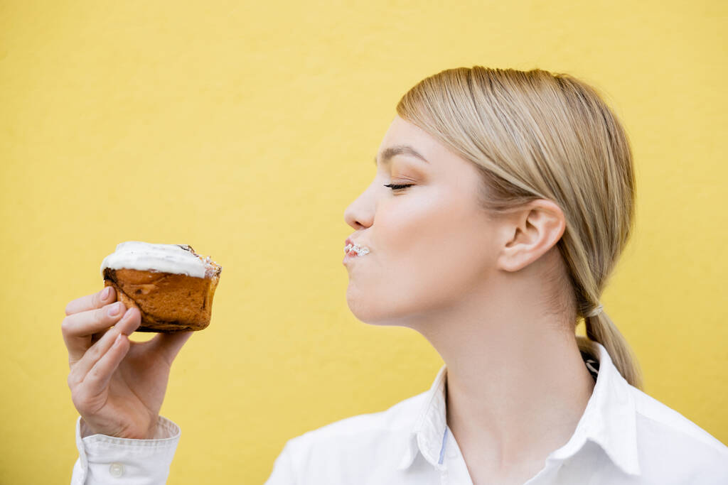 блондинка насолоджується смачним кексом ізольовано на жовтому
 - Фото, зображення