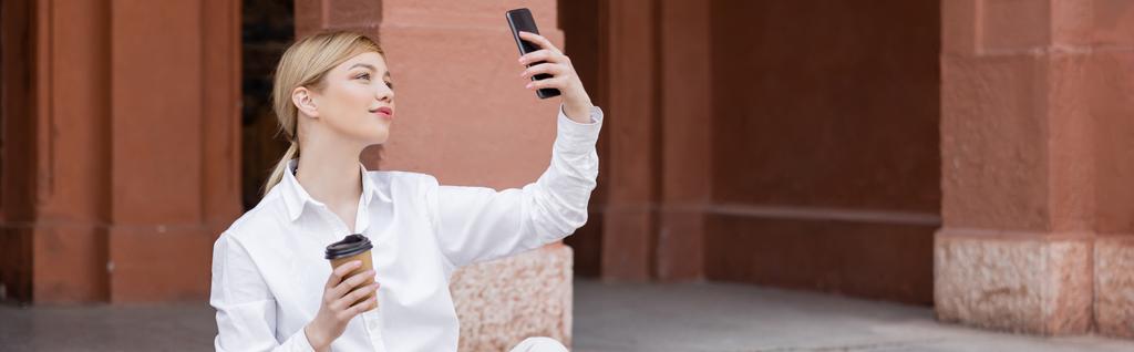 γοητευτική γυναίκα με takeaway ποτό λήψη selfie σε εξωτερικούς χώρους smartphone, πανό - Φωτογραφία, εικόνα