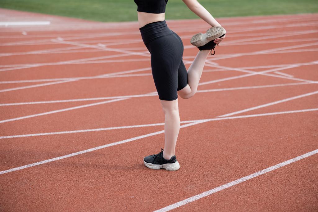 Ausgeschnittene Ansicht einer Sportlerin in schwarzen Fahrradhosen, die Bein auf Stadion streckt - Foto, Bild
