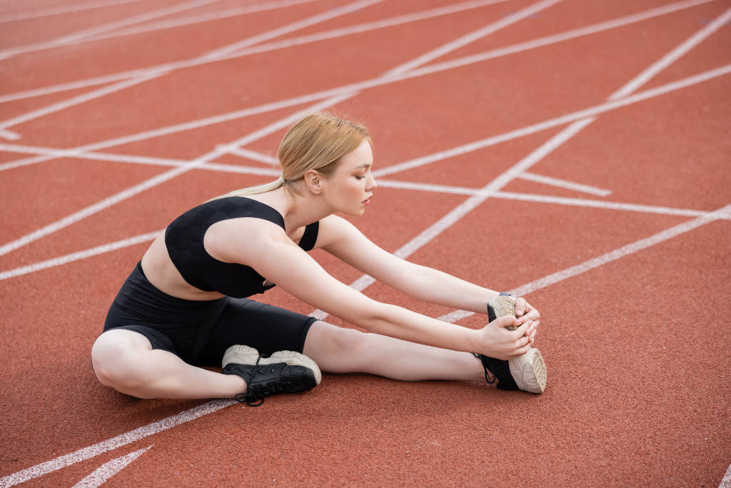 full length view of sportswoman stretching while sitting on stadium - Photo, Image