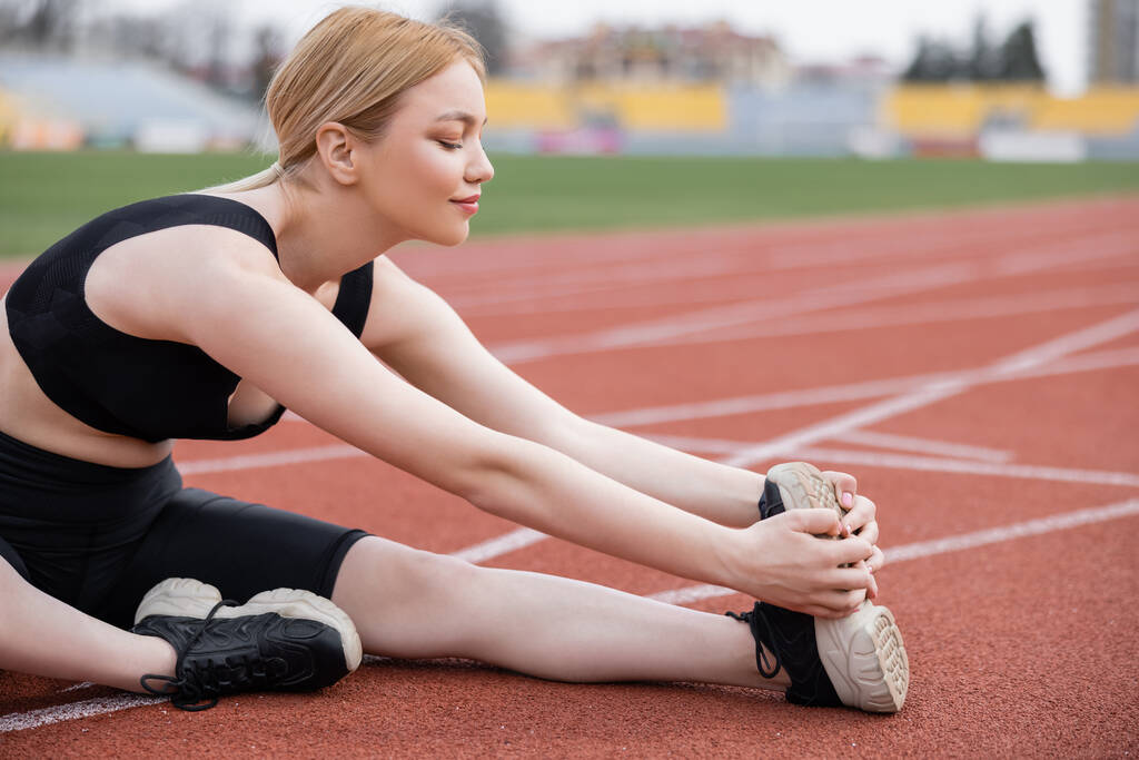 молода спортсменка розтягує ногу, сидячи на стадіоні
 - Фото, зображення