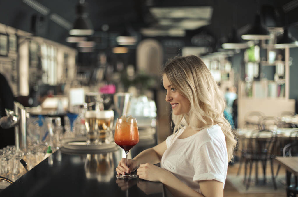 Μια νεαρή γυναίκα στον πάγκο ενός μπαρ πίνει ένα κοκτέιλ. - Φωτογραφία, εικόνα