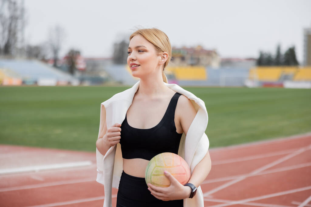 smiling sportswoman holding ball and looking away outdoors - Photo, Image