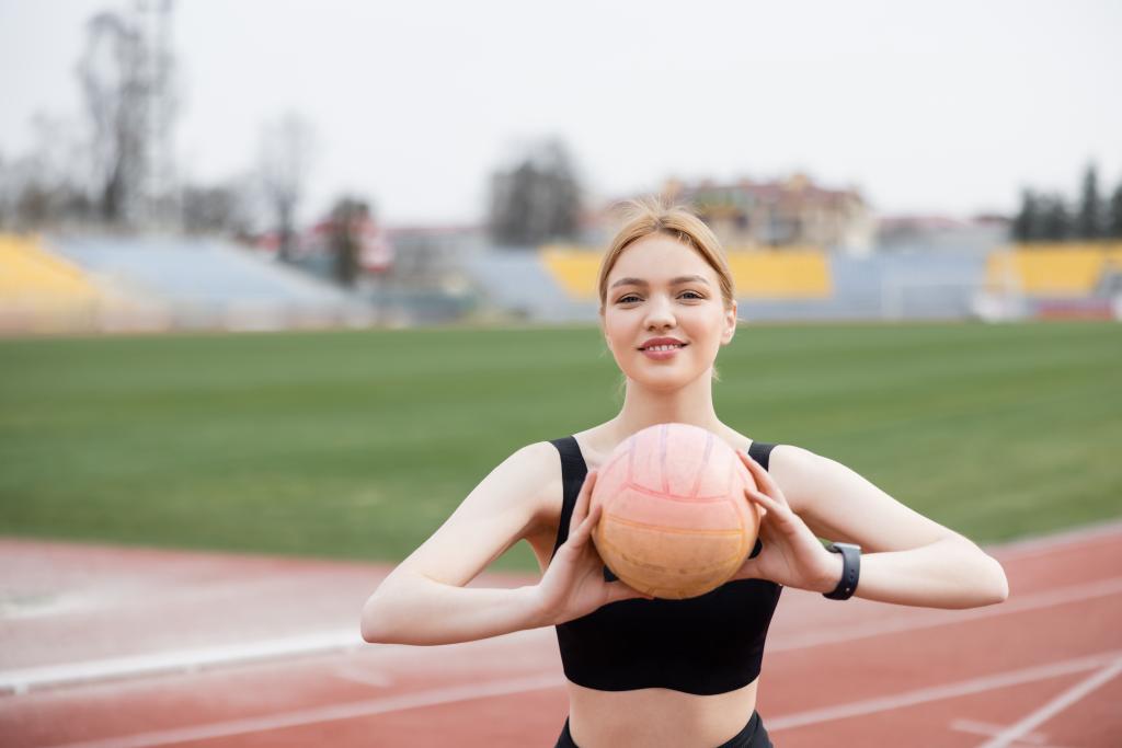 vidám sportos nő néz kamerába edzés közben labdával a szabadban - Fotó, kép