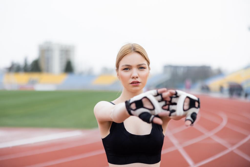 bonita mujer en sujetador deportivo negro y guantes de fitness calentando al aire libre - Foto, imagen